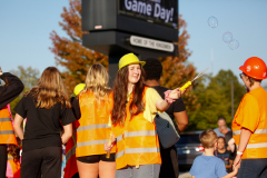 People in orange vests and hard hats at a parade, some blowing bubbles.