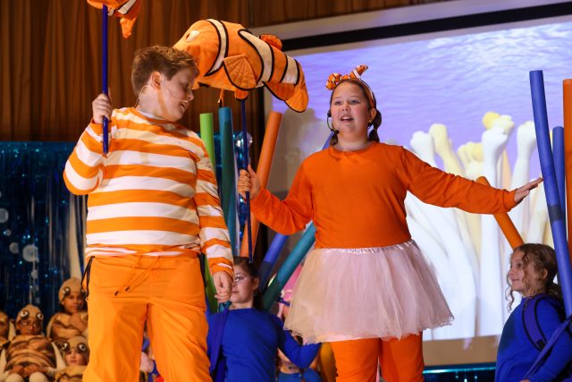 Two children dressed in Finding Nemo costumes, one in orange and white striped swimsuit and the other in a pink tutu, standing on stage