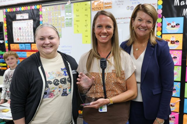 Three people standing in front of a classroom display board, posing for a picture.