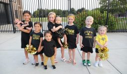 Young cheerleaders posing in front of a fence.