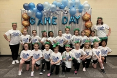A group of young girls in white shirts posing for a picture in front of a balloon arch at a sports event.
