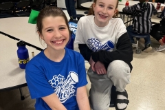 Two young girls posing in a school cafeteria for a photo, both wearing blue and white shirts.