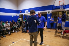 Two men in a gymnasium, one standing on chair, interacting with each other during an event.