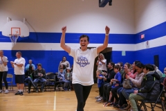 Woman in white shirt and black shorts running on basketball court, celebrating with arms raised.