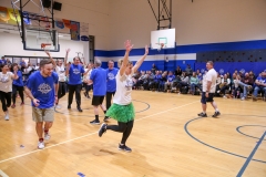People gathered in a gymnasium for a basketball game, some are playing while others watch from the sidelines.