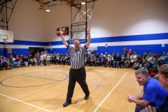 Referee in gymnasium holding trophy, celebrating victory, surrounded by spectators.