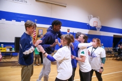 Group of people in a gymnasium celebrating a victory, with one person holding another in their arms and others surrounding