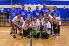 Team of people wearing blue shirts standing in front of a gymnasium.