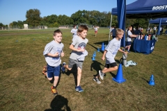 Three children running in a field during a fun run event.