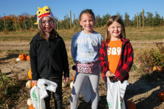 Three children standing in a field of pumpkins, smiling at the camera.