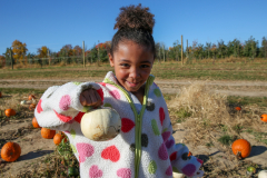 Young girl holding a pumpkin in an orchard.