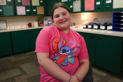Girl in pink shirt sitting at desk in classroom.