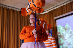 Girl in orange dress holding fish balloon.