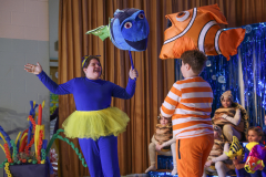 Two people in costumes on stage, one holding a fish balloon, the other a clownfish balloon.