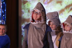 A group of children dressed in shark costumes, performing on stage.