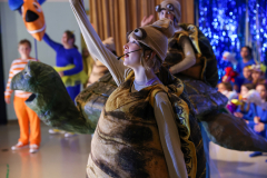 A woman in a costume, standing on a stage, holding a microphone, in front of a group of people.