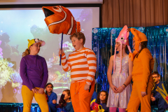 Children in costumes on stage, one holding a fish, performing the show Finding Nemo