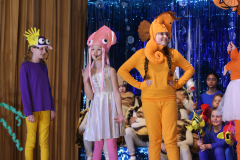 Two people in costumes, standing on stage in front of an audience.