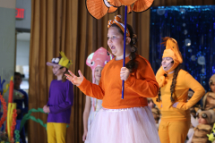Girl in orange costume holding a fish like an umbrella on stage.