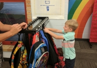 Little boy in school uniform on first day of kindergarten, reaching for a colorful backpack.