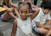 Little girl in a classroom on her first day of kindergarten, smiling at the camera.