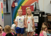Two children standing in front of a colorful backdrop, posing for a picture on their first day of kindergarten.