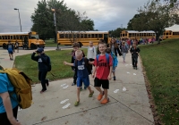 Children walking on sidewalk towards school buses.