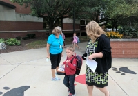 Three people walking on a sidewalk near a school building.