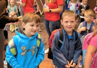 Two young boys in school uniforms standing next to each other wearing backpacks.