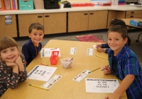 Children sitting at a table in a classroom, smiling at the camera, ready for their first day of kindergarten.