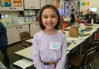 Young girl standing in front of a classroom desk.