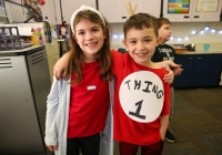Two children posing in a classroom, one wearing a red shirt with "Think" written on it and the other in a black and white