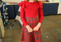 Girl in red dress standing in classroom, smiling at camera.