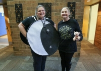Two women posing in front of a moon sign, one holding a stuffed animal, both dressed as characters from the "Mor" book