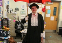 Woman posing in a classroom holding an umbrella with a red top and black handle. She is wearing a white shirt and a black