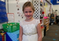Girl in a white dress posing for a picture in a classroom.