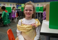 Little girl in princess costume sitting at a table in classroom.
