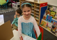 Little girl in princess dress standing at desk in library.
