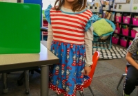 Girl in a red, white, and blue dress standing at a table.