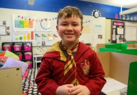 Young boy in a classroom setting, dressed as Harry Potter, standing in front of a desk.