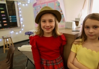 Two young girls posing in a classroom setting, one wearing a red dress and the other in yellow.