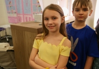Two children standing in front of a classroom desk.