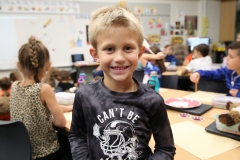 Boy standing in front of classroom, smiling at camera.