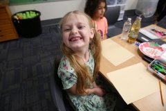 Little girl sitting at desk in classroom, smiling at camera.