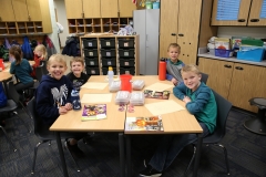 Children sitting around a table in a classroom, smiling at the camera.