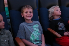 Three children sitting in a movie theater watching a film.