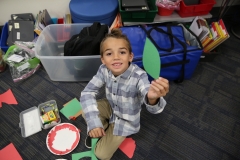 Young boy holding a green leaf in a classroom setting.