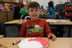 Young boy sitting at a table in front of a plate of cookies.