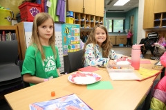 Two young girls sitting at a table in a classroom, engaged in an activity together during a pen pal meet up day.