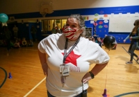 Woman in gymnasium wearing face mask and red star t-shirt.